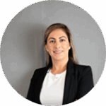 Retrato profesional de una mujer con cabello liso castaño claro, vestida con chaqueta negra y blusa blanca, posando frente a una pared gris.