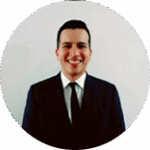 Retrato profesional de un hombre joven con cabello corto, usando traje oscuro y corbata, sonriendo frente a fondo blanco.