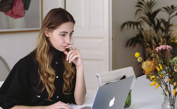Mujer trabajando en un laptop en un escritorio, con la mano en el mentón, en un entorno tipo home office con un florero a un costado.
