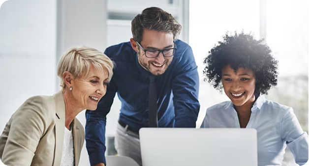 Tres profesionales colaboran frente a un computador portátil en una oficina, revisando información y sonriendo durante una reunión de trabajo en equipo.