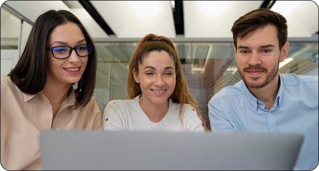Tres profesionales observan una pantalla de computador y colaboran en una reunión de trabajo dentro de una oficina moderna.